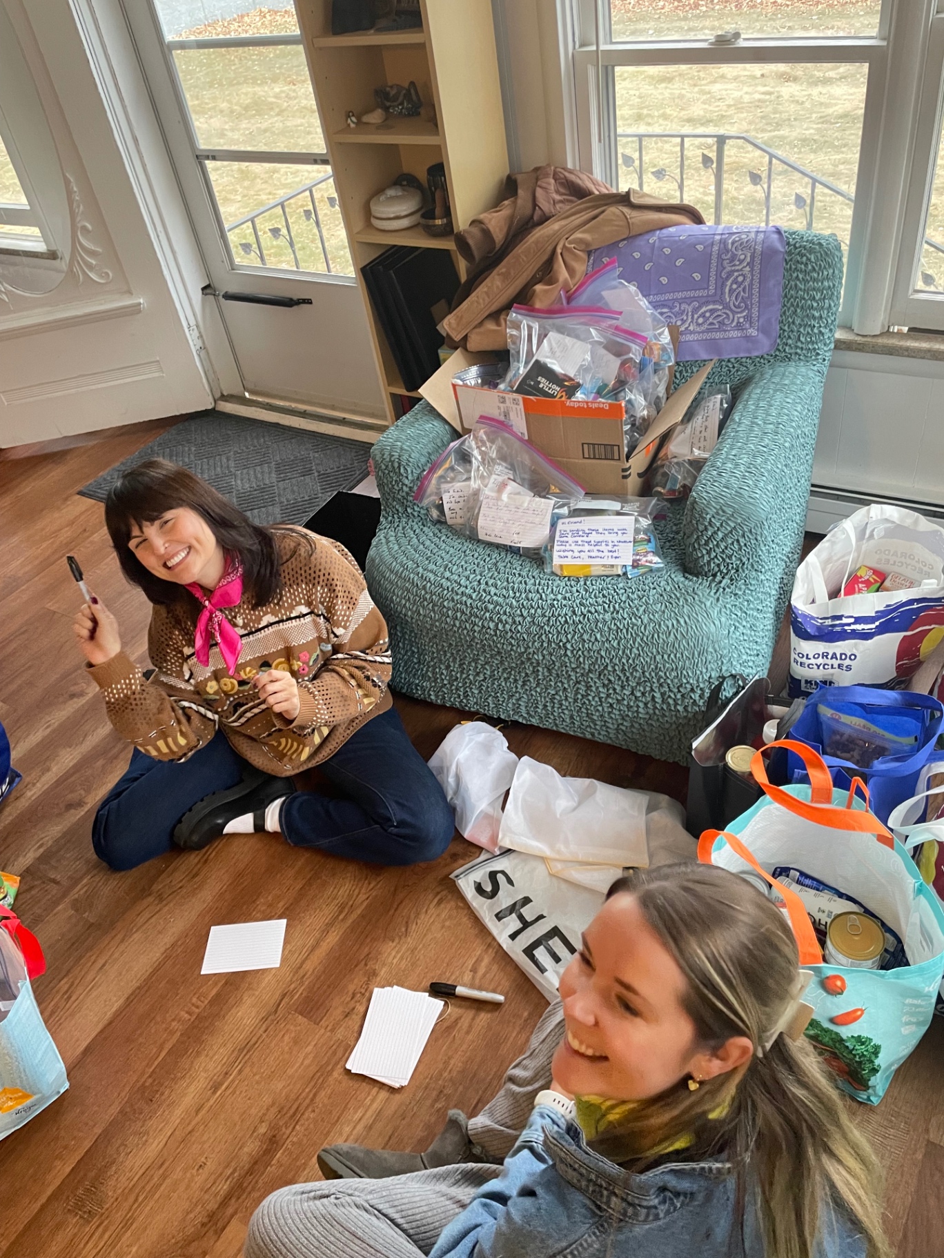 Two volunteers smiling while writing handwritten notes for care packages