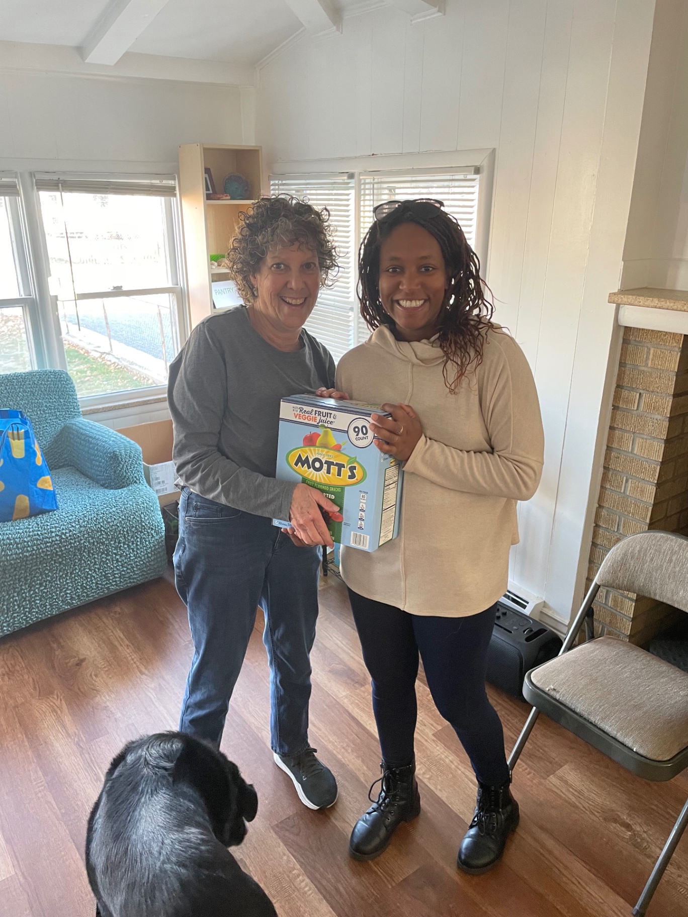 Two neighbors holding a large box of donated fruit snacks
